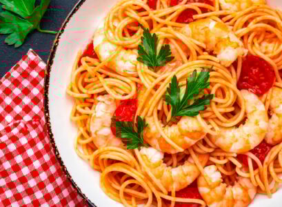 Cooked spaghetti pasta with big shrimp and tomato sauce, black table background, top view