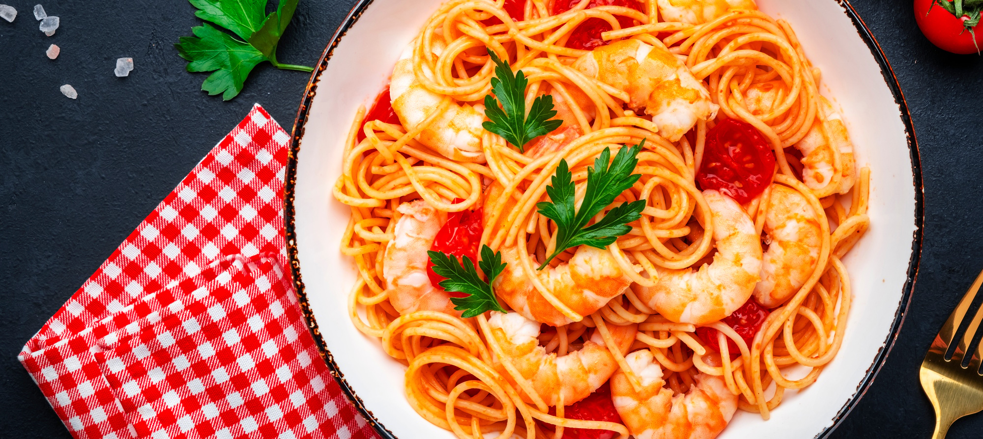 Cooked spaghetti pasta with big shrimp and tomato sauce, black table background, top view