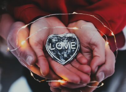 Hands holding stone heart with love text. Blurred background