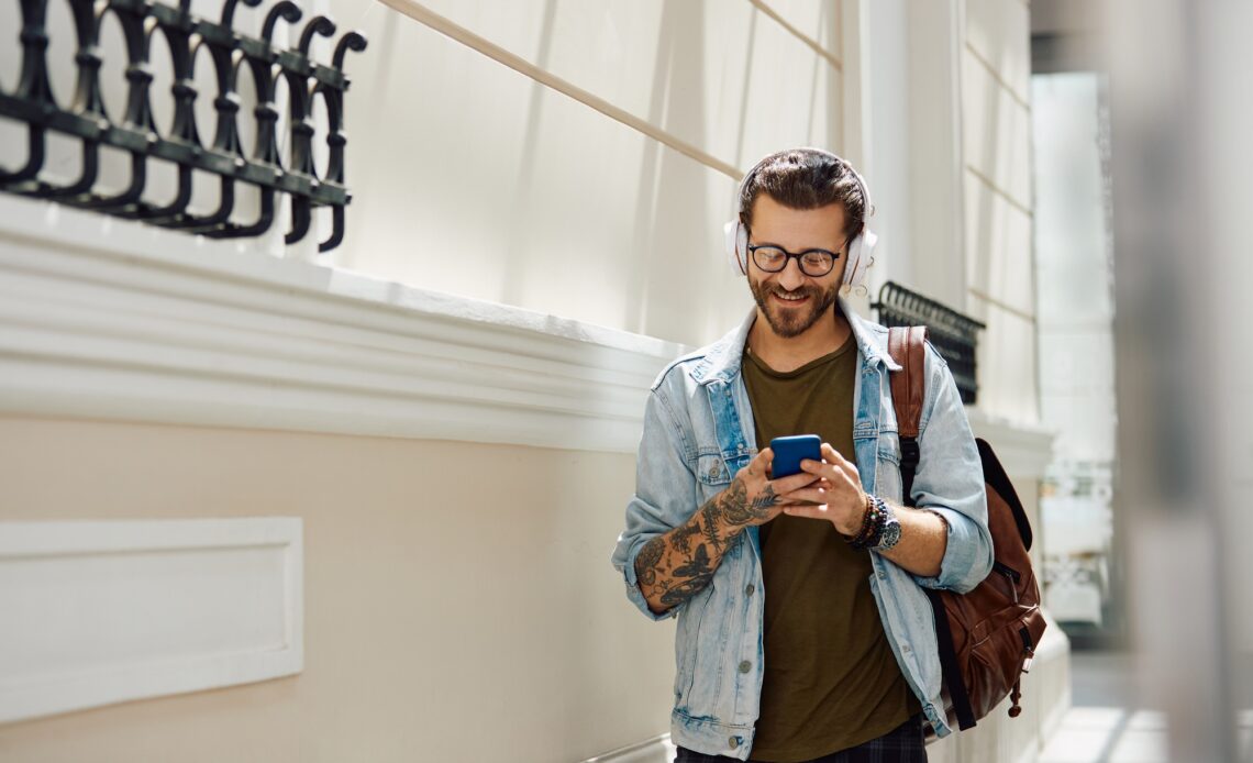 Young happy man text messaging on mobile phone while walking down the hall at the university.