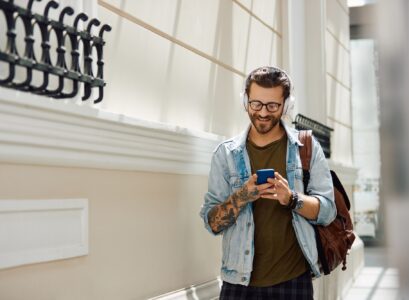 Young happy man text messaging on mobile phone while walking down the hall at the university.